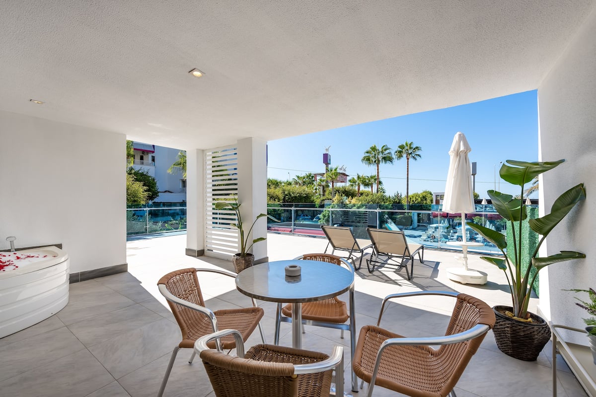 A rooftop terrace with a pool, wicker furniture, and a view of the city.