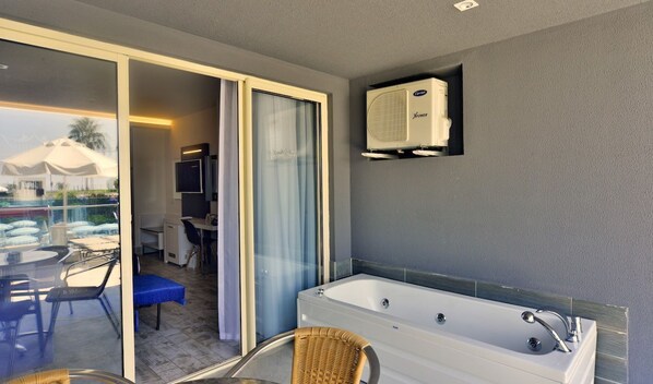 Un baño moderno con una bañera grande, cabina de ducha con mampara de vidrio y aire acondicionado instalado en el techo.