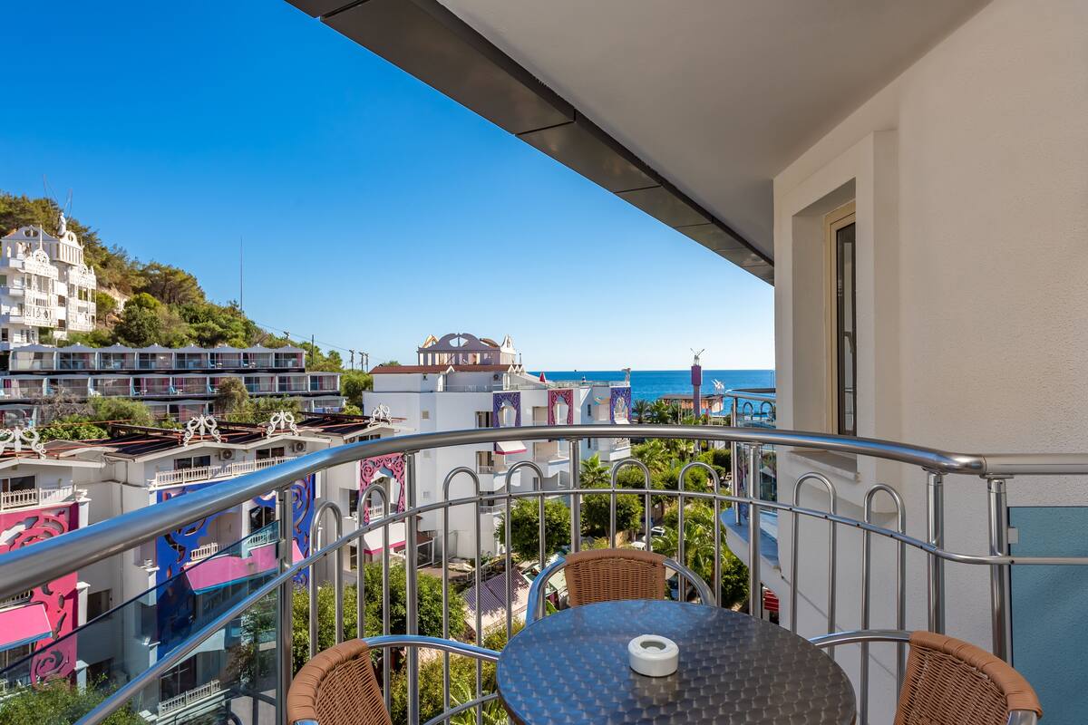 A balcony with a table and chairs, overlooking a coastal area with buildings and a view of the sea.