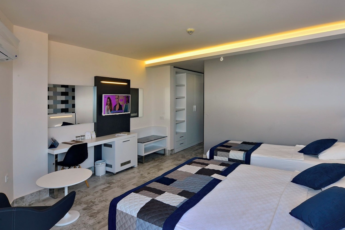 Una habitación de hotel con escritorio, dos camas, televisor y diseño moderno.