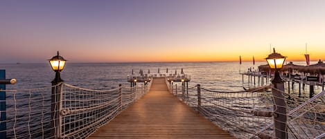 A wooden pier with rope railings and street lamps, leading to a dock with umbrellas.