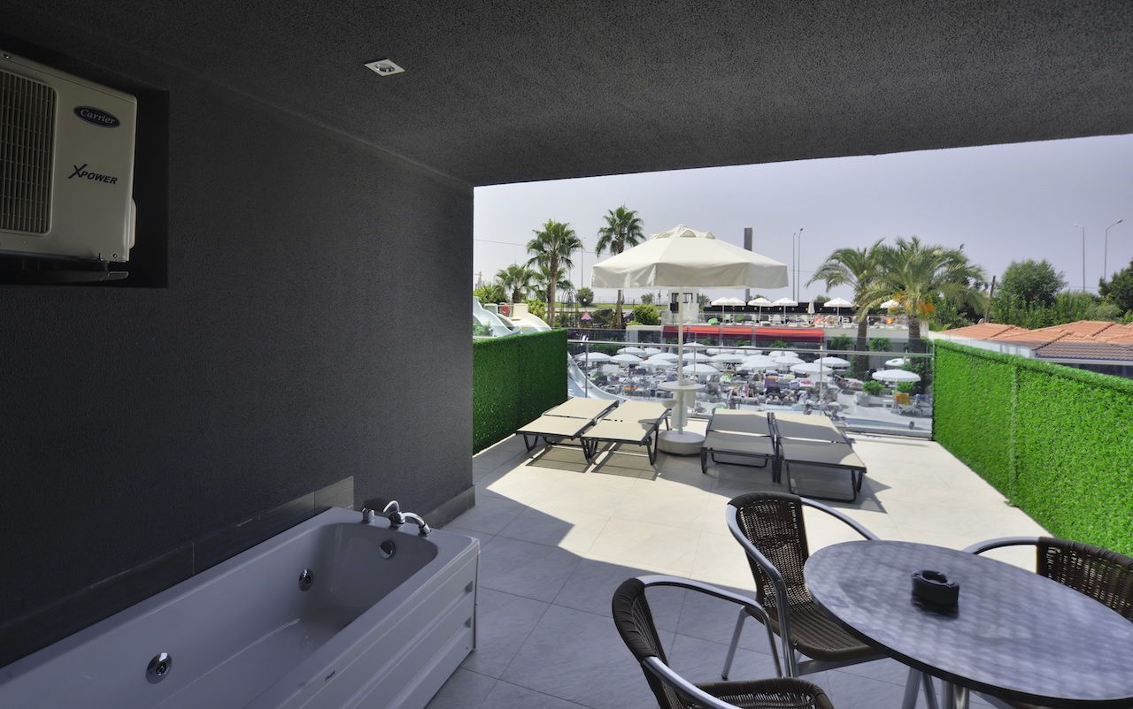 A modern bathroom with a bathtub and a shower, a balcony with outdoor seating, and a view of a pool area.