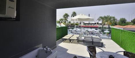 A modern bathroom with a bathtub and a shower, a balcony with outdoor seating, and a view of a pool area.