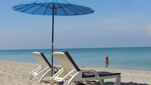 Uma praia com duas cadeiras de praia brancas e um guarda-sol azul.