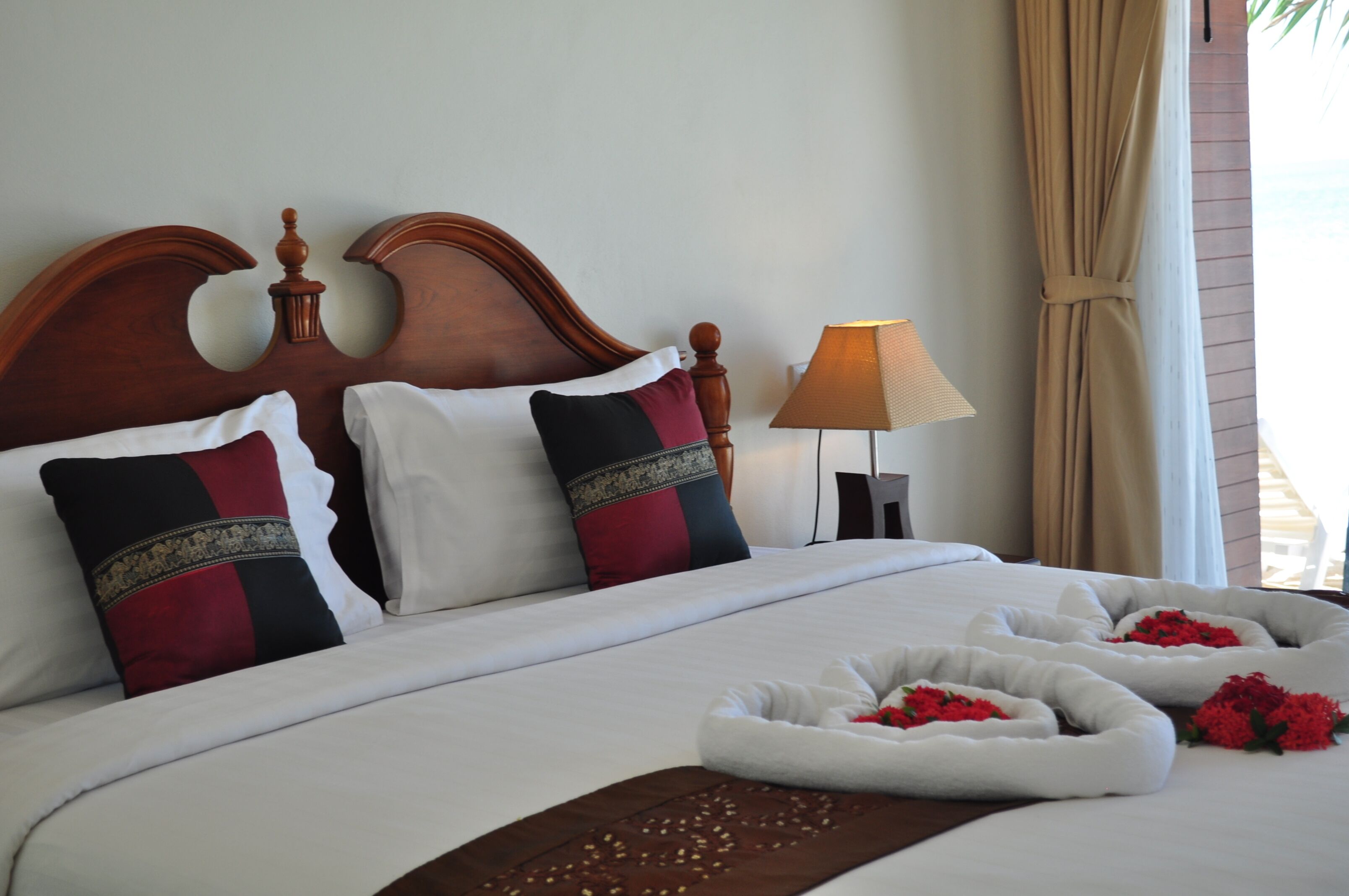Una cama impecable con almohadones decorativos, una lámpara de noche y arreglos florales.