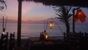 Uma área de refeições à beira-mar com uma mesa posta para dois, uma vela e um candeeiro.