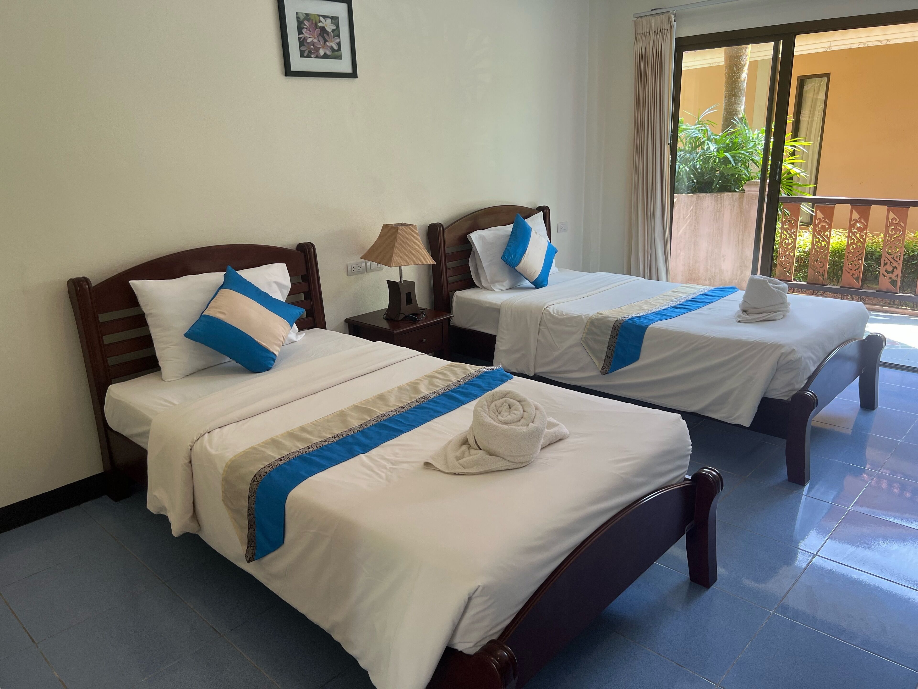 A hotel room with two beds, each with a blue and white bedspread, a wooden headboard, and a small bedside table with a lamp.