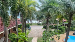 Um resort tropical com um caminho pavimentado, palmeiras, uma piscina e um edifício com telhado vermelho.