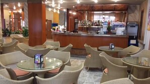Un hall d'hôtel avec des fauteuils et des tables en osier, un bar et un comptoir de réception.