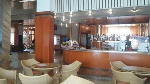 Un hall d’hôtel comprenant un bar, des fauteuils en osier et un comptoir d’accueil.