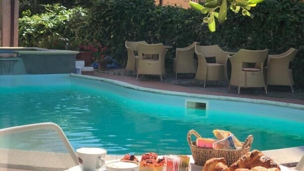 Une table placée au bord de la piscine, recouverte d’une nappe à motifs floraux, avec un panier de pain et un croissant.