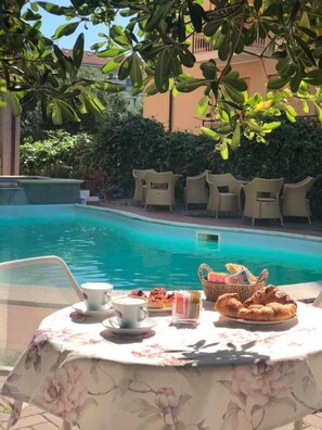 Una mesa junto a la piscina con un mantel estampado y una cesta de pan, además de un croissant.