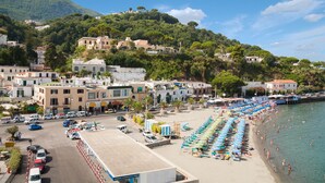 A coastal town with a beach lined with umbrellas and boats, buildings on a hillside, and a clear sky. - Hotel Gran Paradiso (Casamicciola Terme)