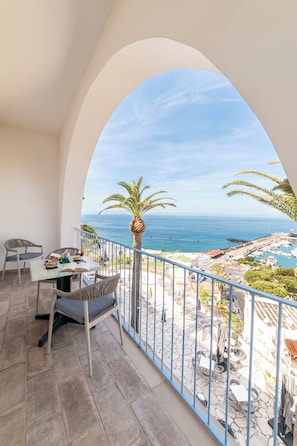 Un balcón con mesa y sillas, vista al mar y una palmera.