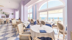 A dining area with round tables, wicker chairs, and a view of the sea. - Hotel Gran Paradiso (Casamicciola Terme)
