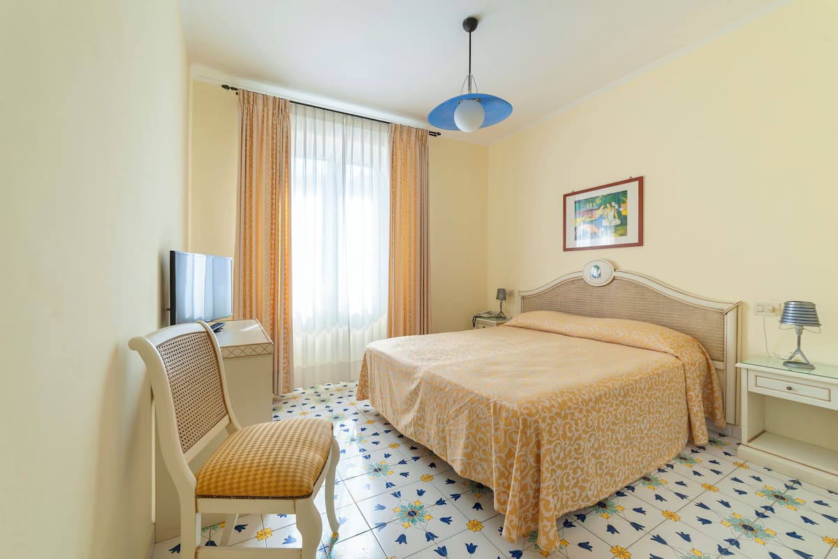 A hotel room with a bed, a chair, a desk, a television, and a window with curtains.