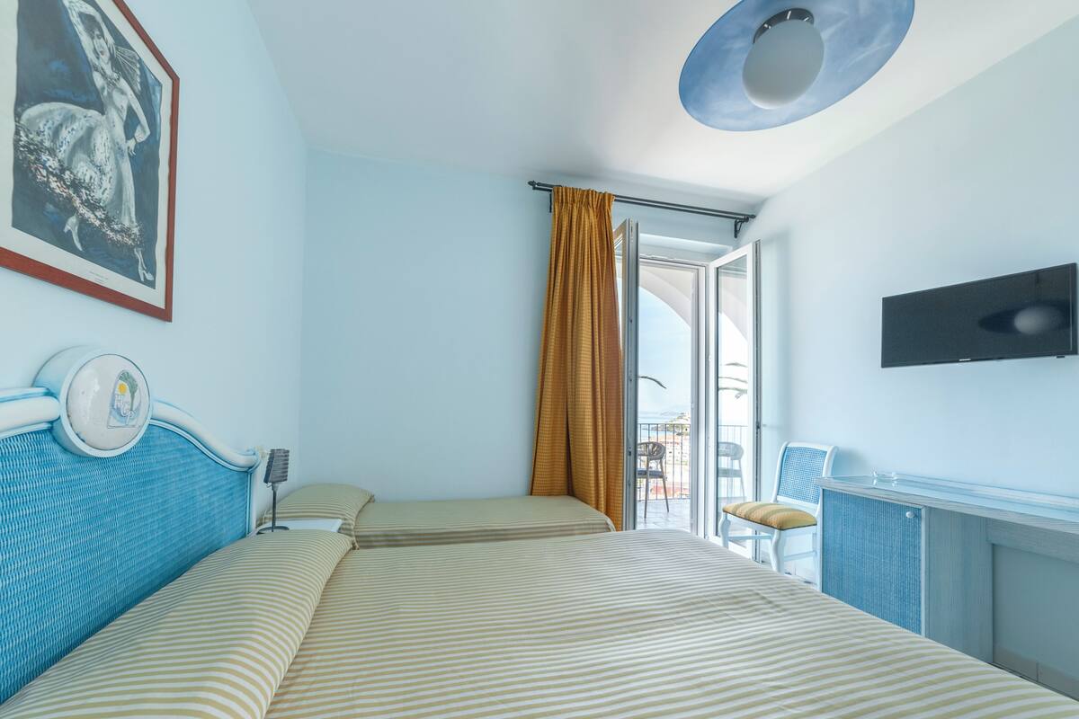 A hotel room with a bed, a chair, a television, and a window with curtains.