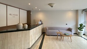 A hotel reception area with a reception desk, a sofa, and a small table. - Hotel Hill House (Bogotá)