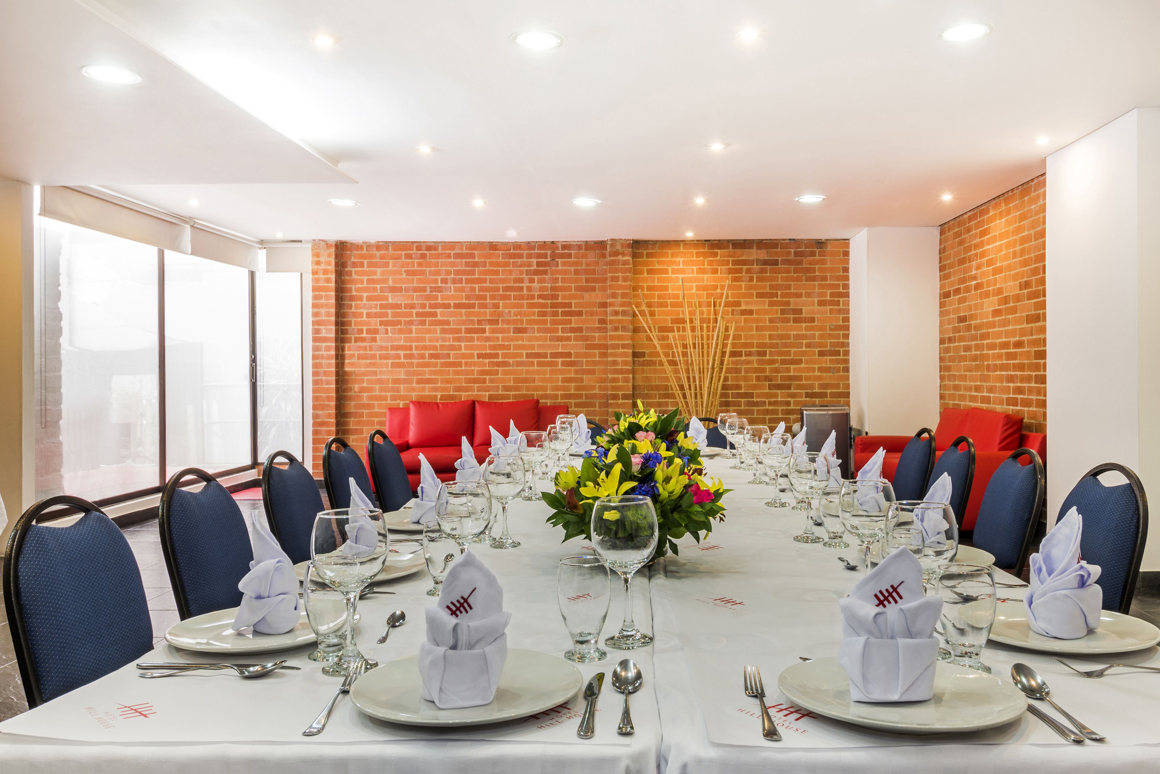 Un salón de conferencias con una larga mesa dispuesta para una reunión, equipado con sillas, platos, cubiertos y un centro de mesa.