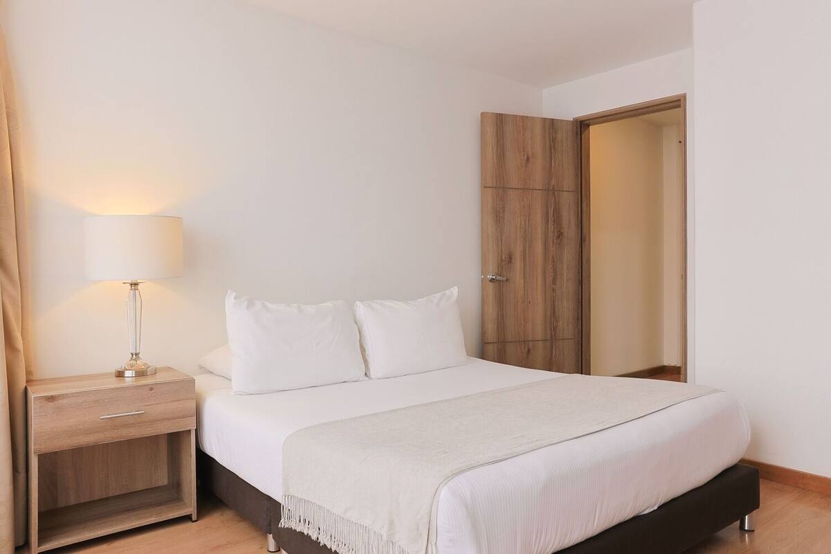 A bedroom with a bed, a nightstand, a lamp, and a wardrobe.