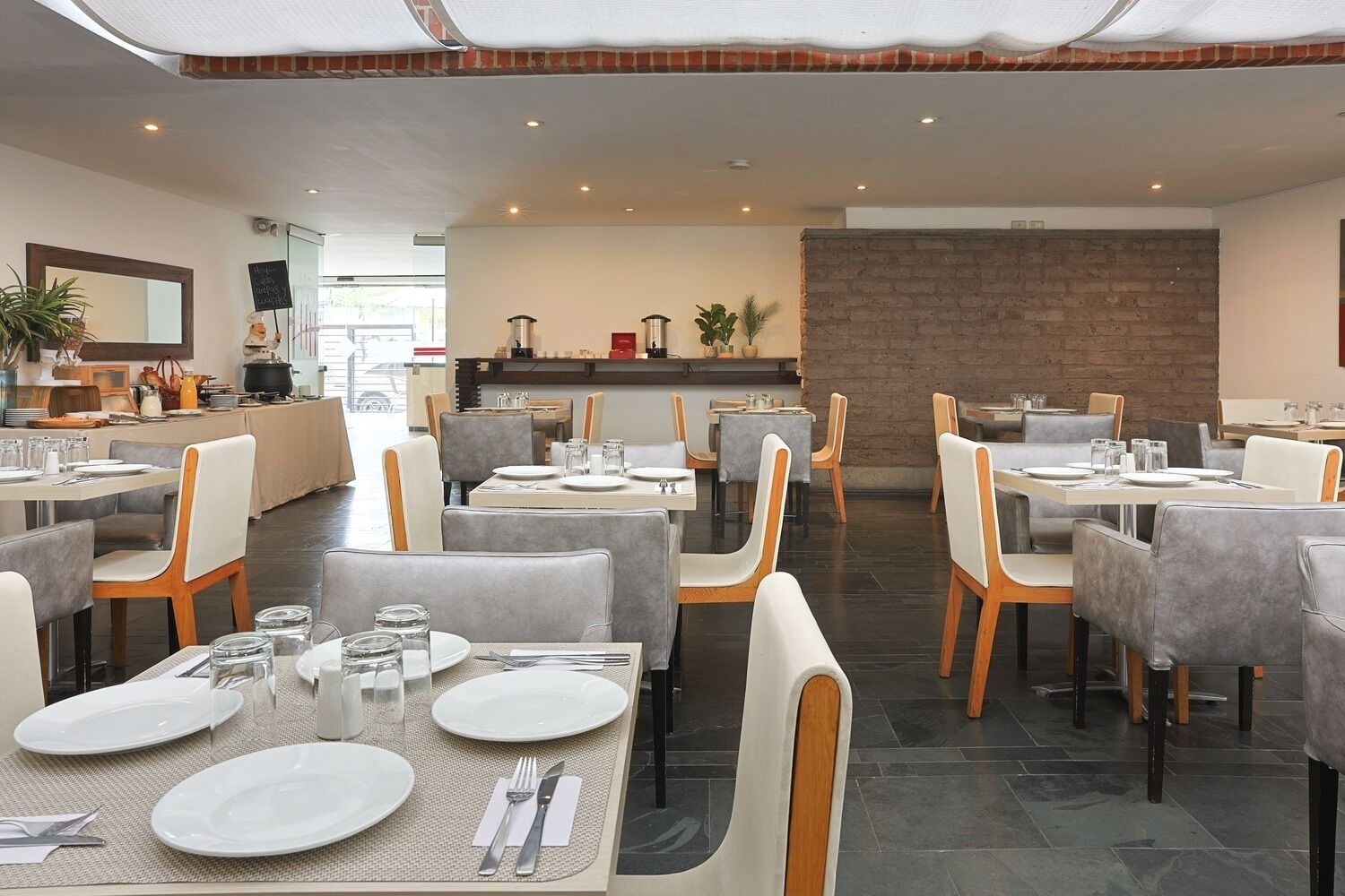 Un restaurante con varias mesas y sillas, un área de cocina al fondo y una pared de ladrillo.