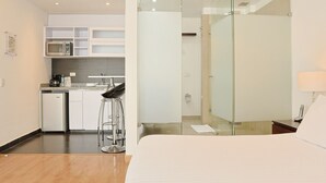 A modern hotel room with a bed, a small kitchenette, a glass shower enclosure, and a bar stool. - Hotel Hill House (Bogotá)