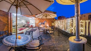An outdoor patio with round tables and chairs, a brick wall, and decorative lights. - Hotel Hill House (Bogotá)