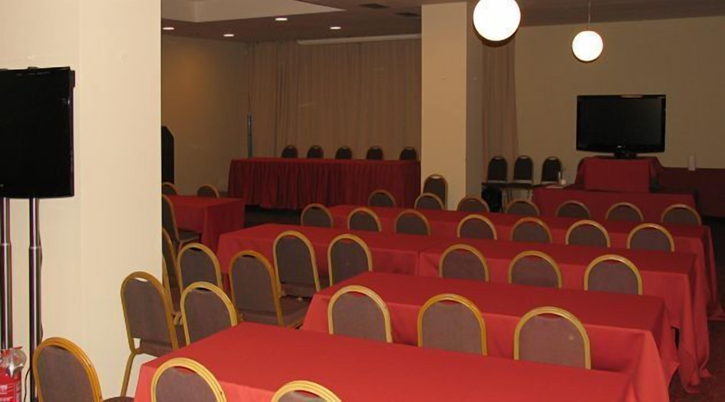 A conference room with rows of tables and chairs, a television screen, and a stage area.