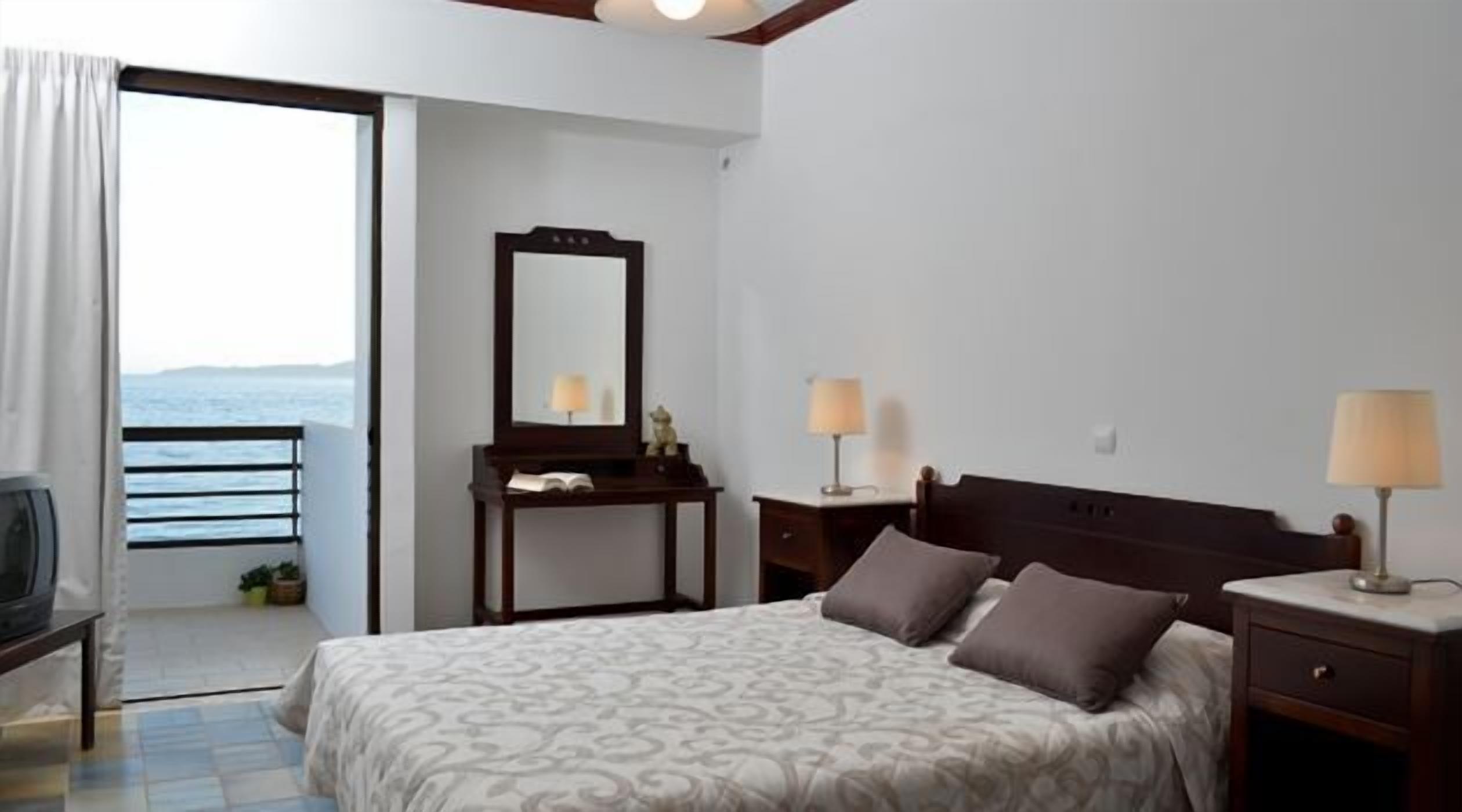 Habitación de hotel con cama, lámparas de noche, cómoda, espejo y vistas al mar.