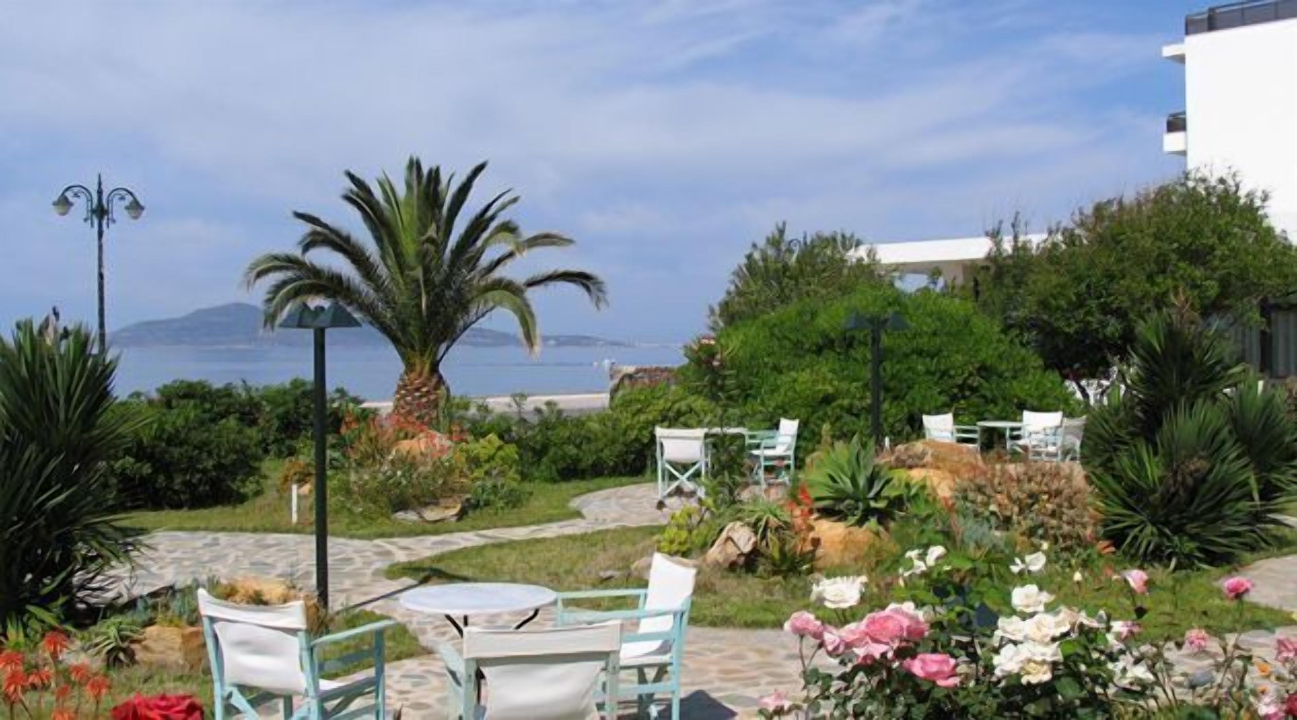 Un área de estar al aire libre con mesas y sillas, rodeada de abundante vegetación y vistas al mar.