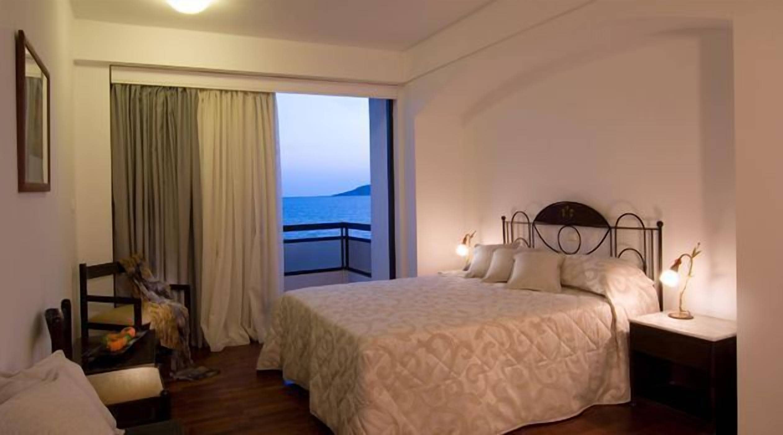 Ein Hotelzimmer mit Bett, Stuhl, Nachttisch und Meerblick durch ein Fenster.