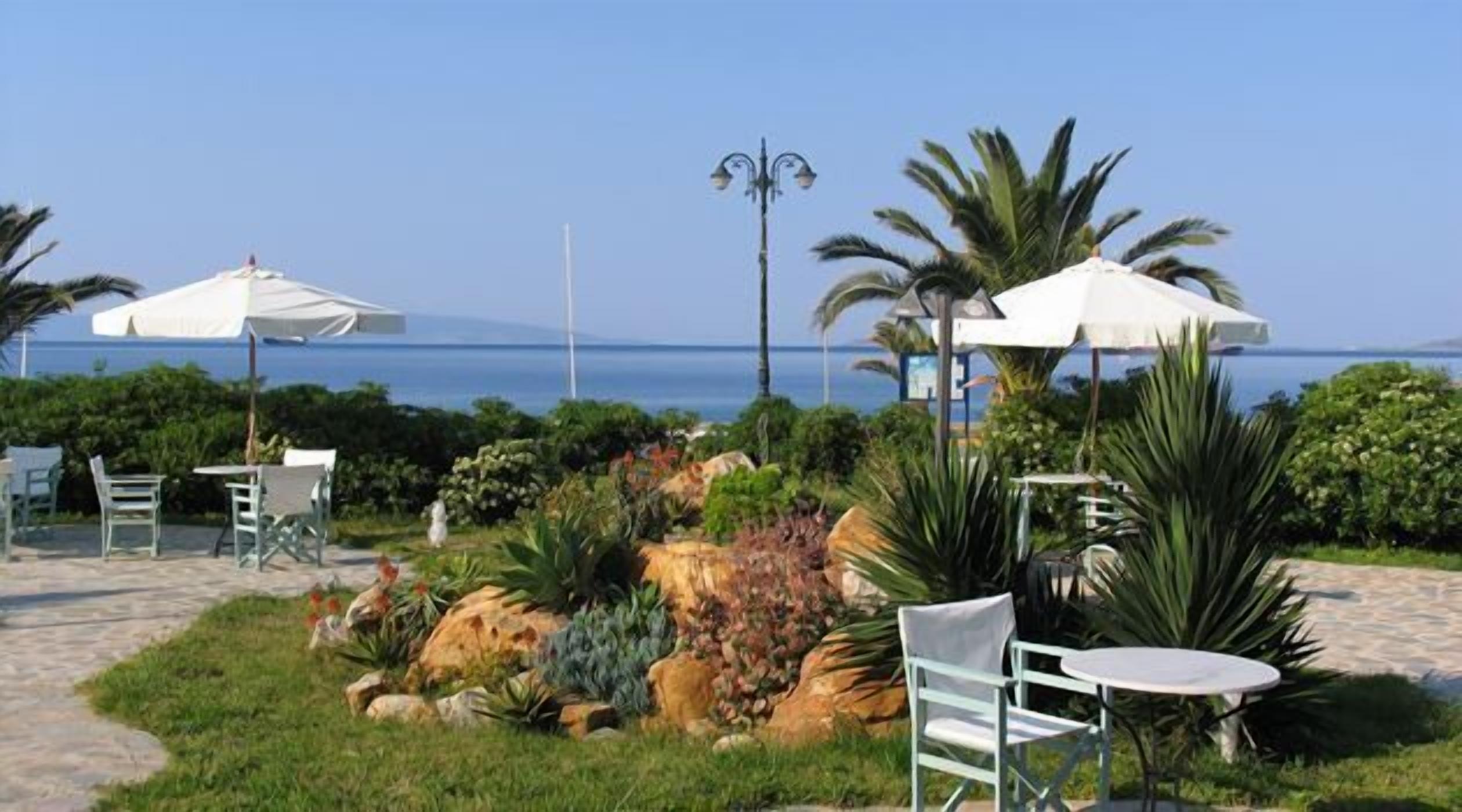 An outdoor seating area with tables and chairs, surrounded by tropical plants and a view of the sea.
