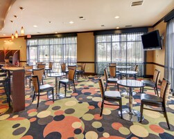 Un hall de hotel con mesas y sillas redondas, una recepción y ventanas grandes con cortinas.
