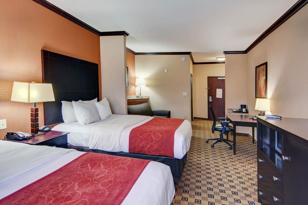 A hotel room with two beds, a desk, a chair, and a dresser.