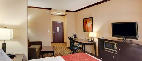 Habitación de hotel con cama, escritorio, silla, televisor y puerta que da a otra habitación.