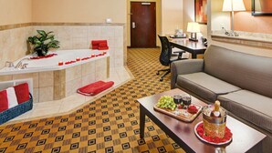 A hotel room with a bathtub, a sofa, a dining table with a tray of food and drinks, and a small table with a bottle and glasses. - Comfort Suites Kilgore (Kilgore)