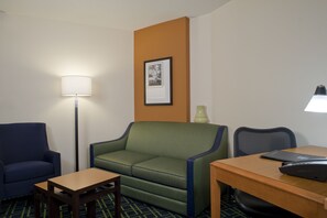 Ett hotellrum med en grön soffa, en blå fåtölj, ett träbord och ett skrivbord med en bärbar dator.