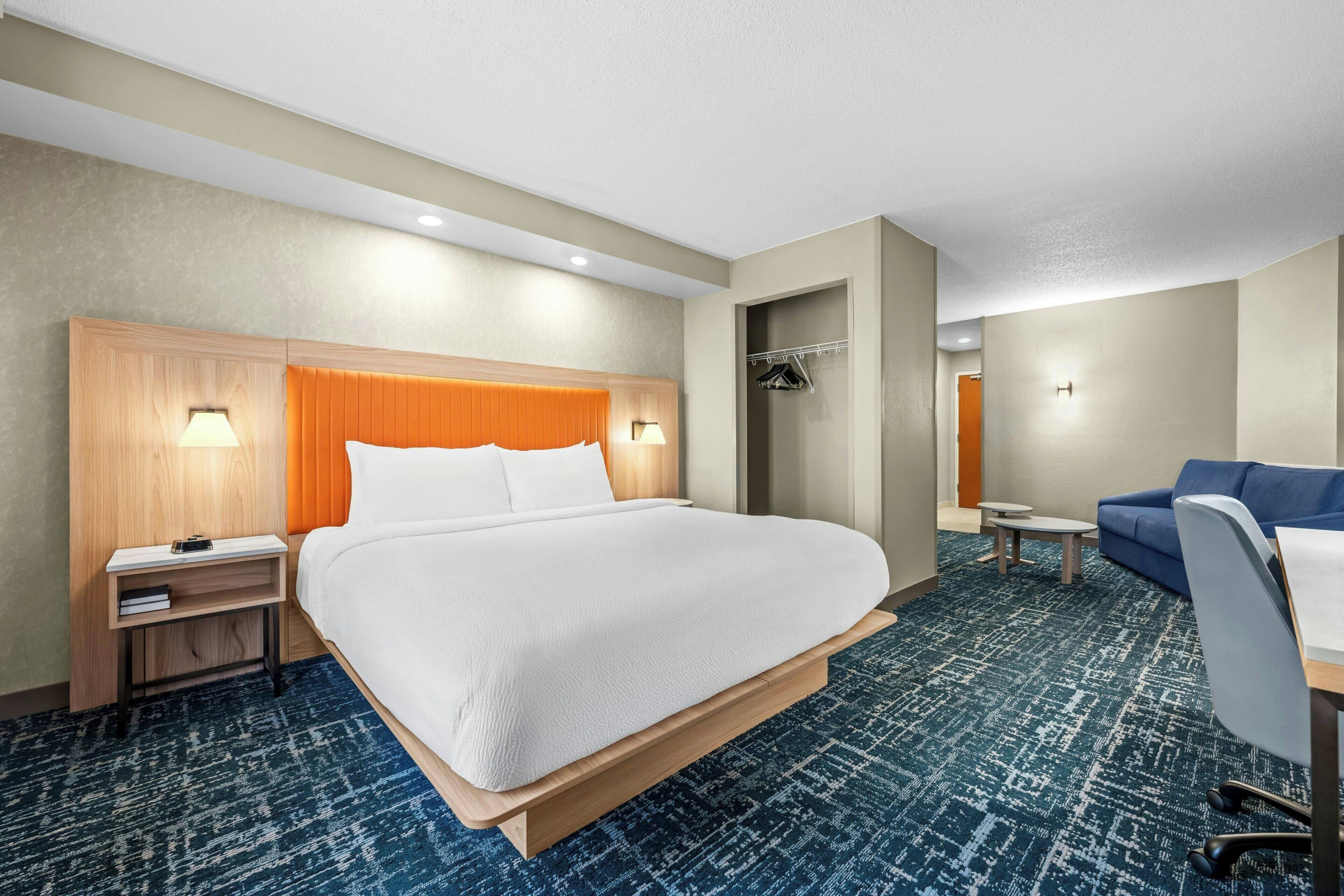 A hotel room with a large bed, a desk, a chair, a wardrobe, and a small table.