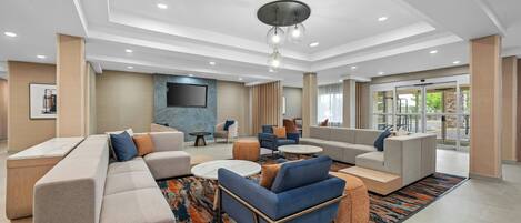 A modern hotel lobby with a sectional sofa, armchairs, a coffee table, and a patterned rug.