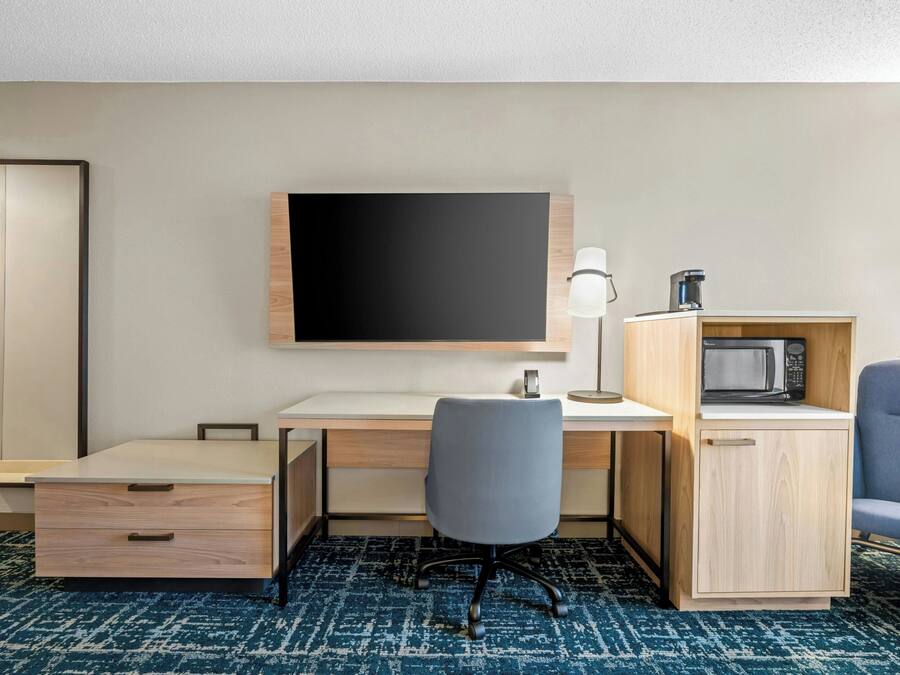 Habitación de hotel con escritorio, silla, televisor de pantalla plana, microondas y un armario.
