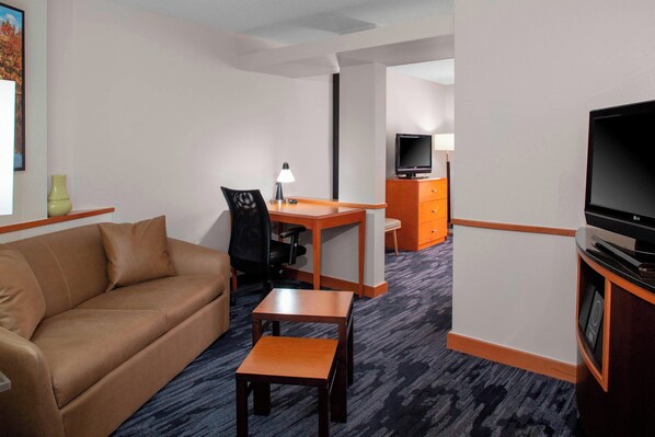 Ett hotellrum med en soffa, ett skrivbord, en stol, en tv och ett litet bord.