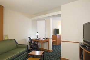 Ett hotellrum med en grön soffa, ett skrivbord med en lampa, en tv och ett litet bord.