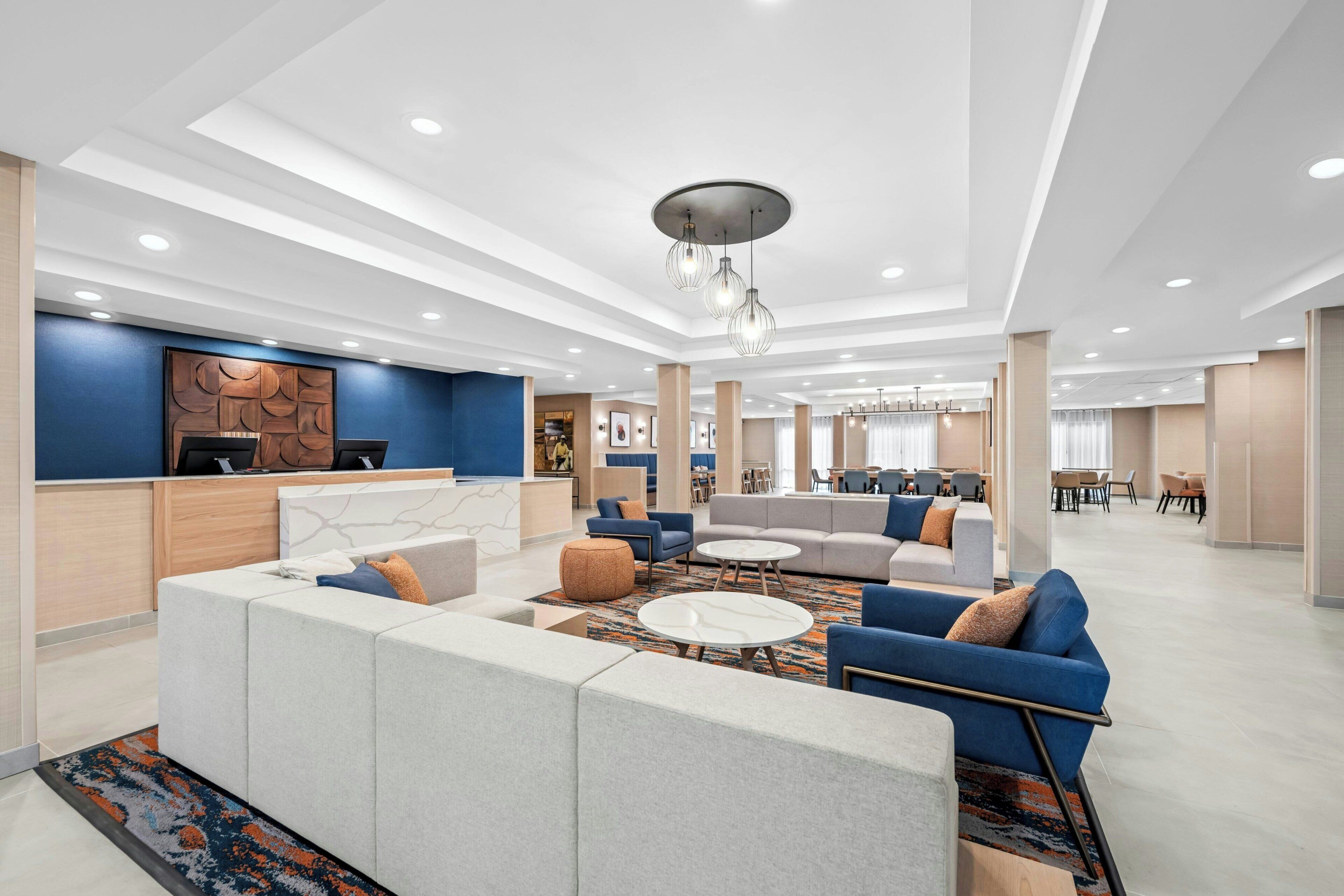 A modern hotel lobby with a reception desk, seating areas, and a dining space.