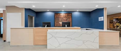 Mostrador de recepción con frente de mármol, paneles de madera y pared azul con diseño de paneles de madera.
