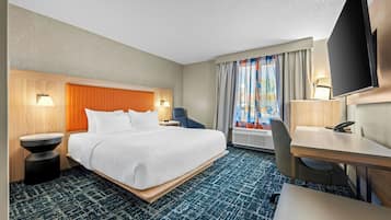 A hotel room with a bed, a desk, a chair, a TV, and a window with curtains.