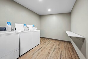 A laundry room with a row of washers and dryers, a wooden floor, and a white shelf. - Fairfield Inn & Suites by Marriott Gadsden (Gadsden)