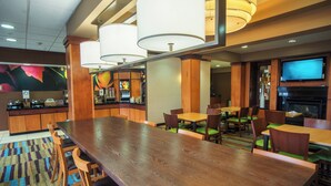 A spacious hotel lobby with a large wooden reception desk, multiple seating areas, a bar, and a television mounted on the wall. - Fairfield Inn & Suites by Marriott Bartlesville (Bartlesville)