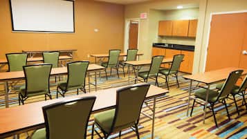 A conference room with tables and chairs, a projector screen, and a kitchen area.