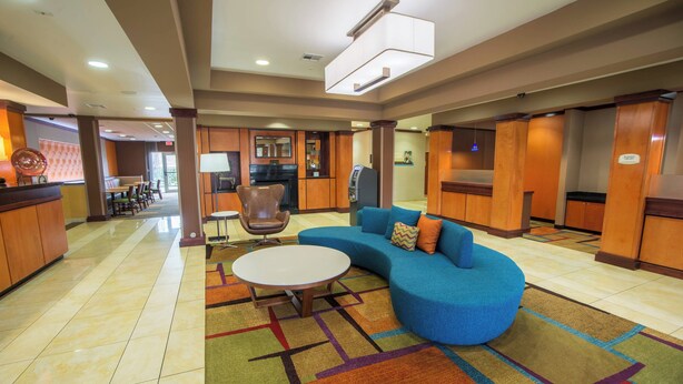 A hotel lobby with a curved blue sofa, a round table, and a patterned carpet. - Fairfield Inn & Suites by Marriott Bartlesville (Bartlesville)
