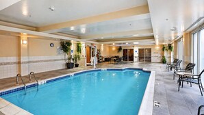 An indoor swimming pool with a tiled edge, surrounded by lounge chairs and tables, and a clock on the wall. - Hilton Garden Inn Ridgefield Park (Ridgefield Park)